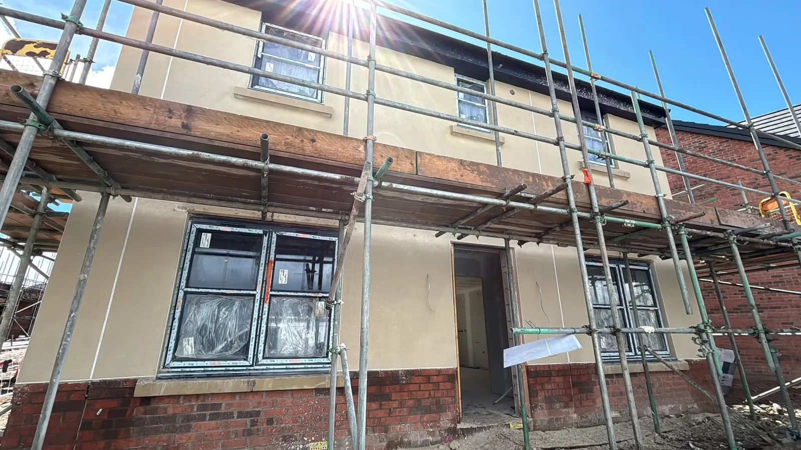 Sand-coloured monocouche render on a new-build house seen from the scaffold
