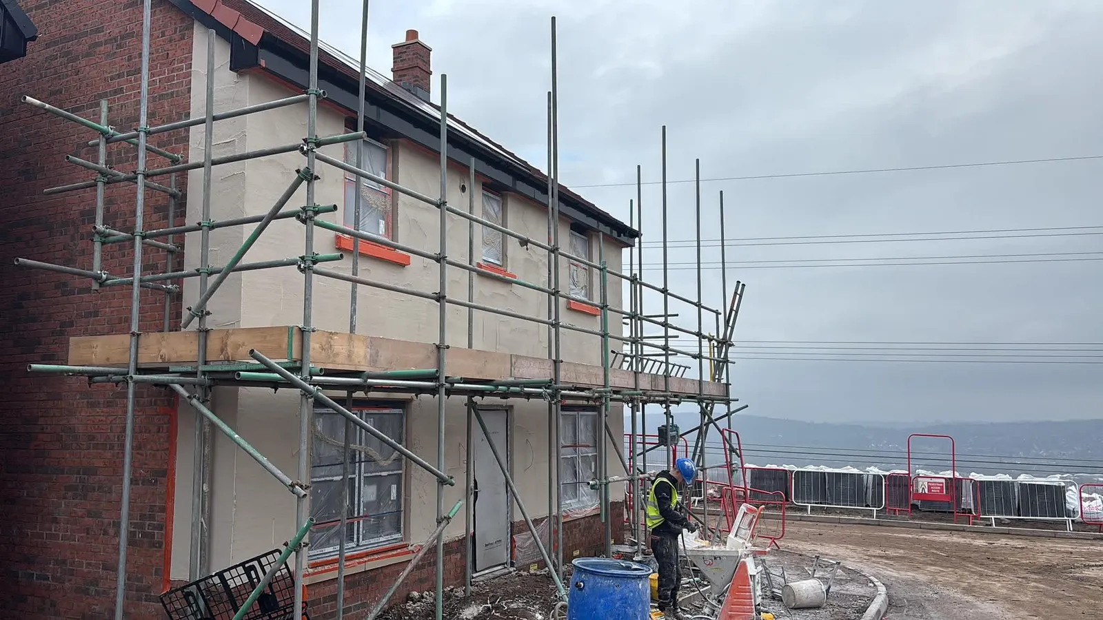 Operative spray-applying render with a render pump on a house under scaffold