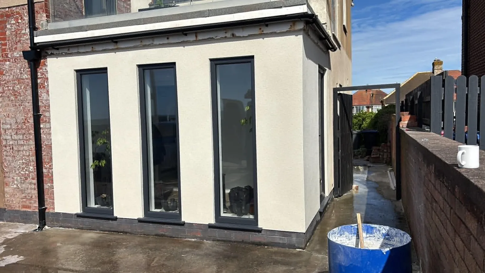 Freshly applied thin-coat render on a single-storey extension with anthracite window frames